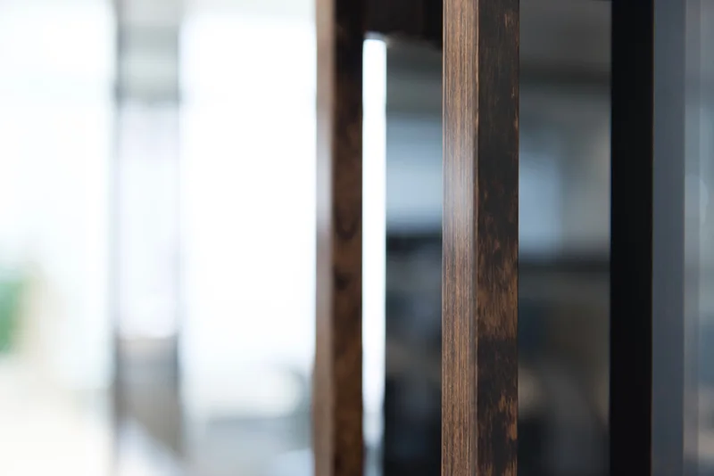 Close-up of dark wood vertical partitions framing a softly blurred, bright modern interior.