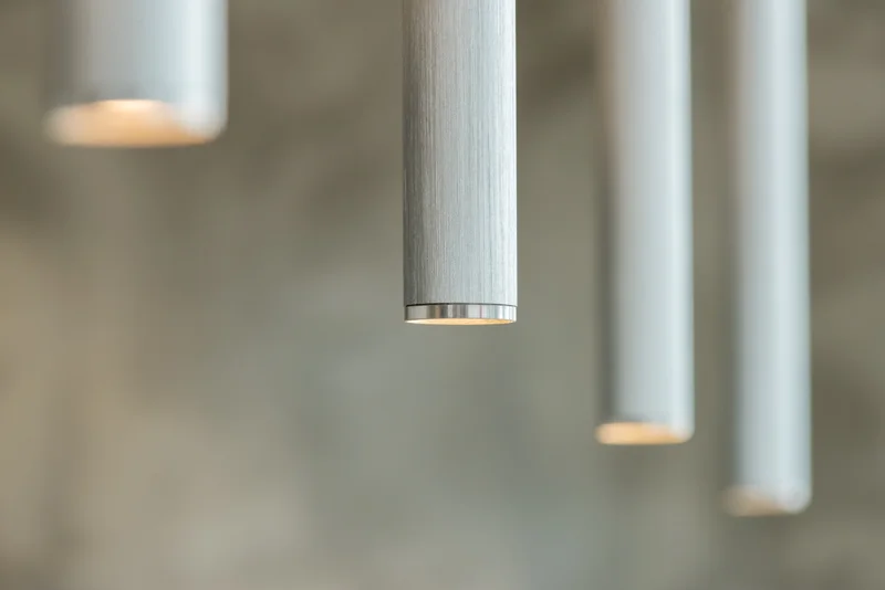 Close-up of cylindrical pendant lights with brushed metal finishes and warm illumination in a softly blurred interior.