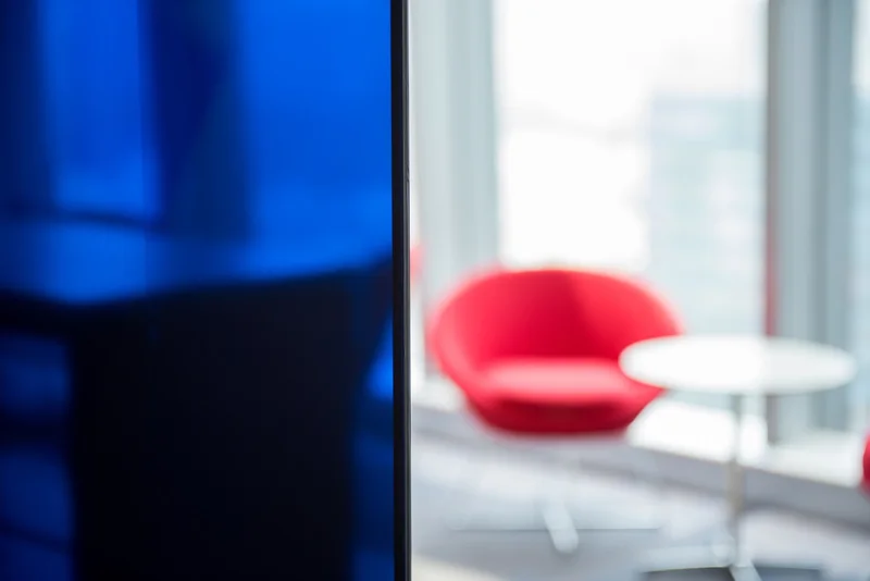 Blurred contemporary office interior with a deep blue partition, red lounge chair, white table, and bright floor-to-ceiling windows.