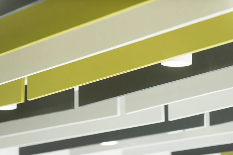 Abstract view of a modern interior ceiling with suspended lime green and white panels, dark accents, and circular recessed lights.