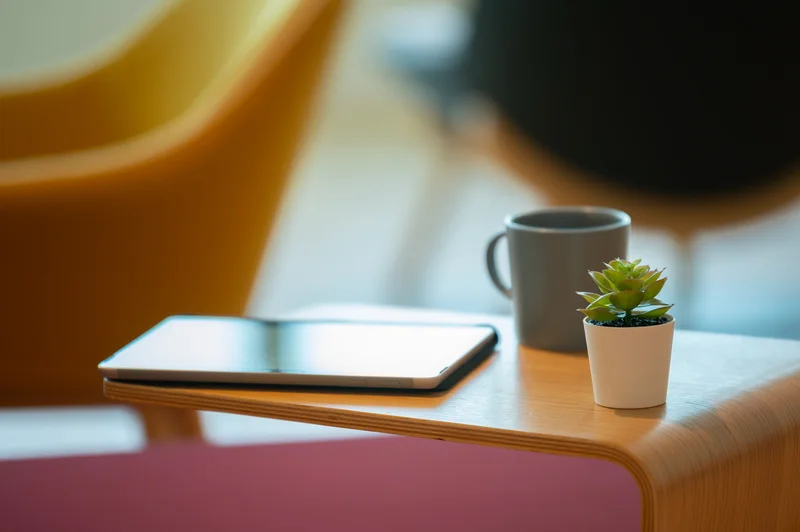Close-up of a tablet, coffee mug and potted succulent on a curved wooden office table.