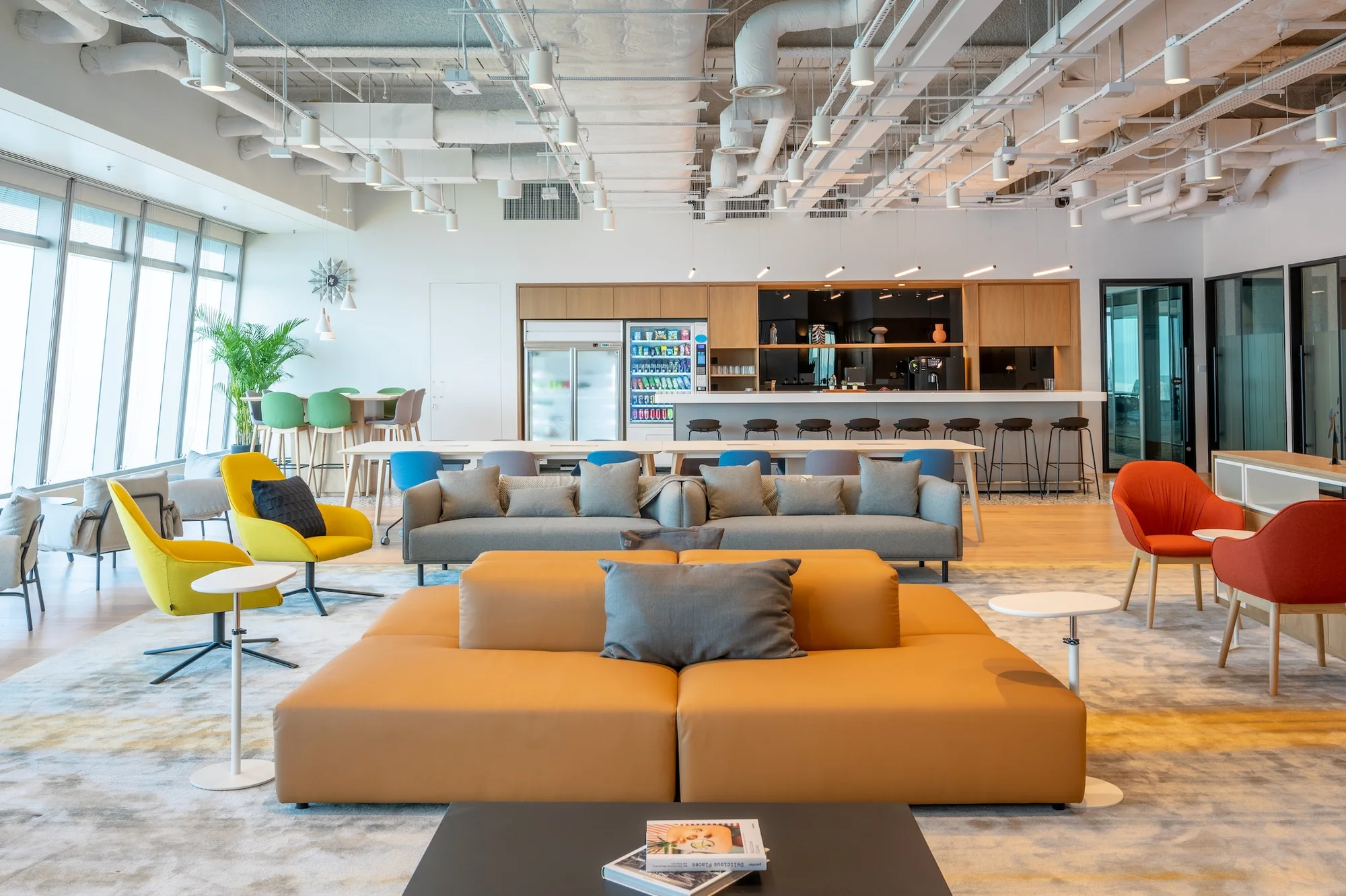 Bright serviced office lounge at ICC Hong Kong with colorful seating, exposed services ceiling, cafe counter, bar stools, and floor-to-ceiling windows.