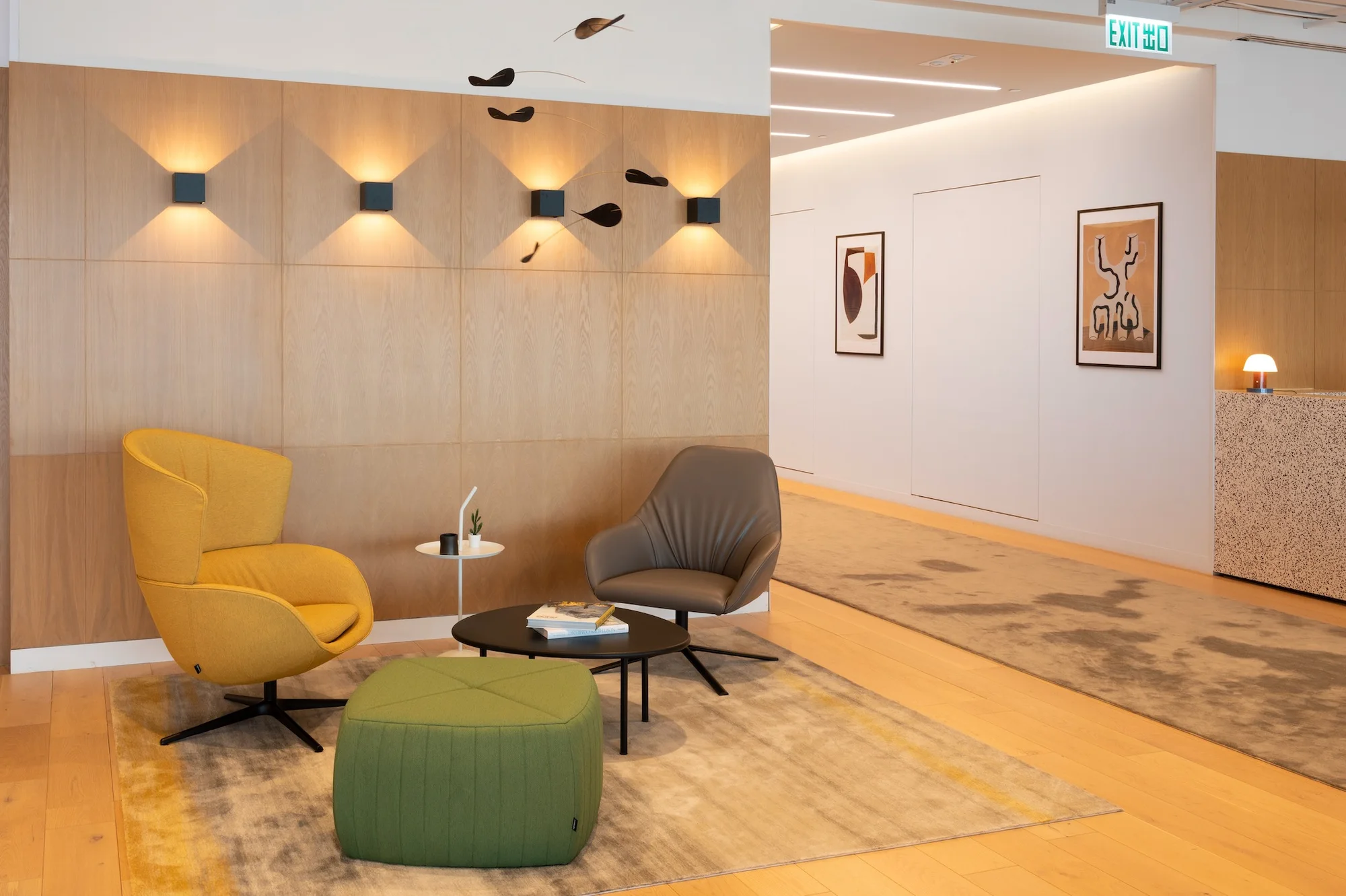 Premium serviced office lounge with wood-paneled walls, colorful lounge chairs, sculptural lighting, artwork, and a terrazzo reception desk.