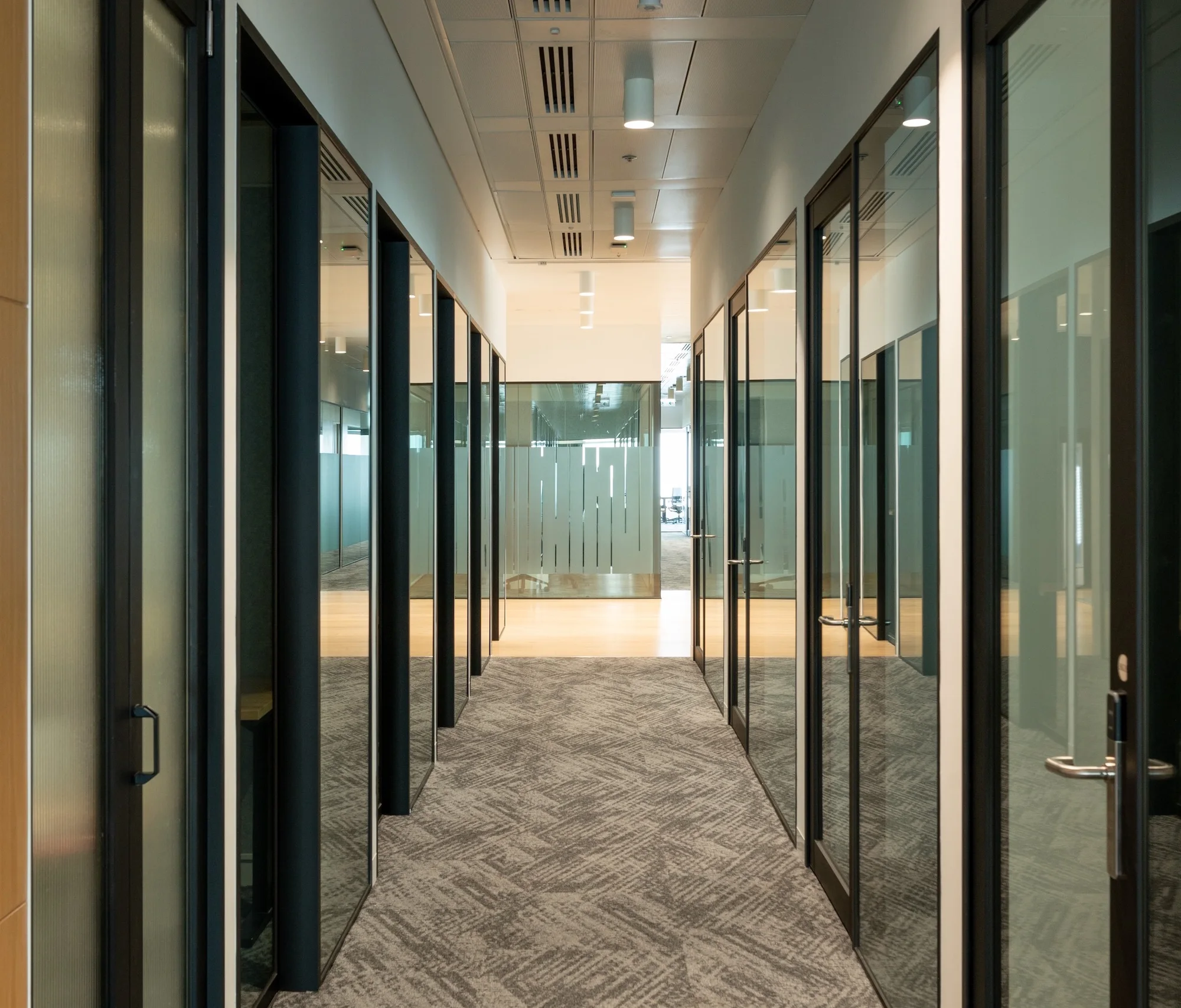Glass-fronted office corridor with black frames, patterned carpet, wood flooring, and suspended lights in ICC Hong Kong.